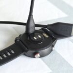 A charging and sync cable is seen going in to the back of a Garmin watch