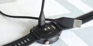 A charging and sync cable is seen going in to the back of a Garmin watch