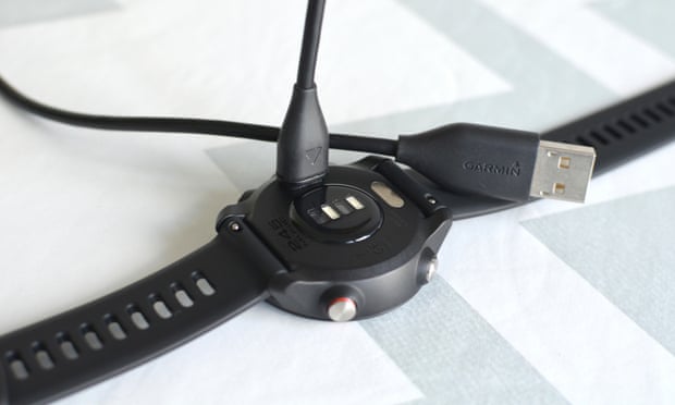 A charging and sync cable is seen going in to the back of a Garmin watch