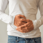 a man in a white shirt and jeans holding the front of his stomach with both hands