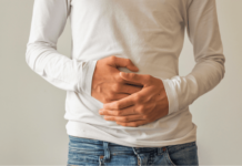 a man in a white shirt and jeans holding the front of his stomach with both hands