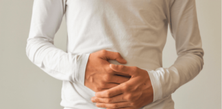a man in a white shirt and jeans holding the front of his stomach with both hands