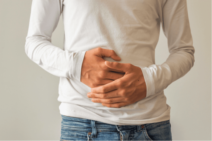 What Causes Intestinal Spasms? - Digestive Healthcare Center a man in a white shirt and jeans holding the front of his stomach with both hands